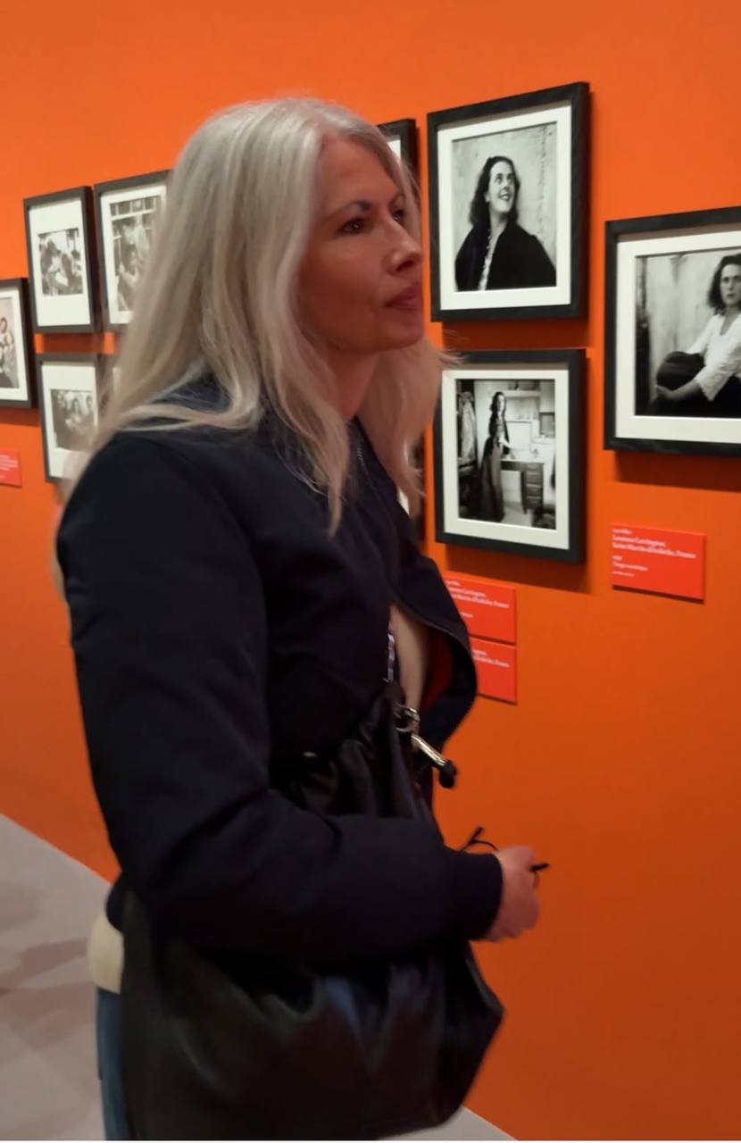Priscilla Caldwell viewing black and white photographs on an orange gallery wall